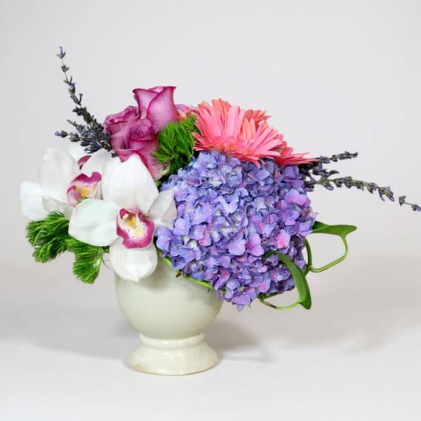 Colorful floral arrangement in a white vase with hydrangea, roses, orchids, and pink blooms