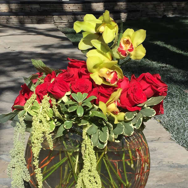 Red roses and yellow orchids in a round glass vase