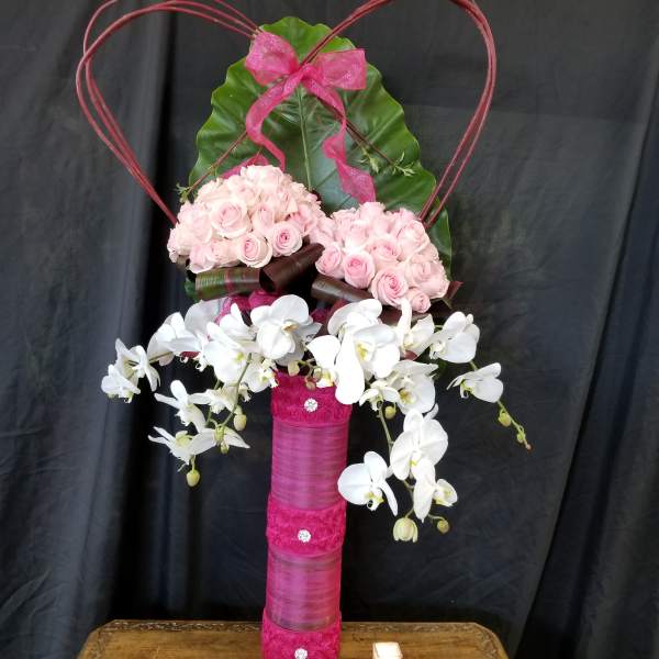 Pink roses and white orchids arranged in a tall decorative vase with a heart frame