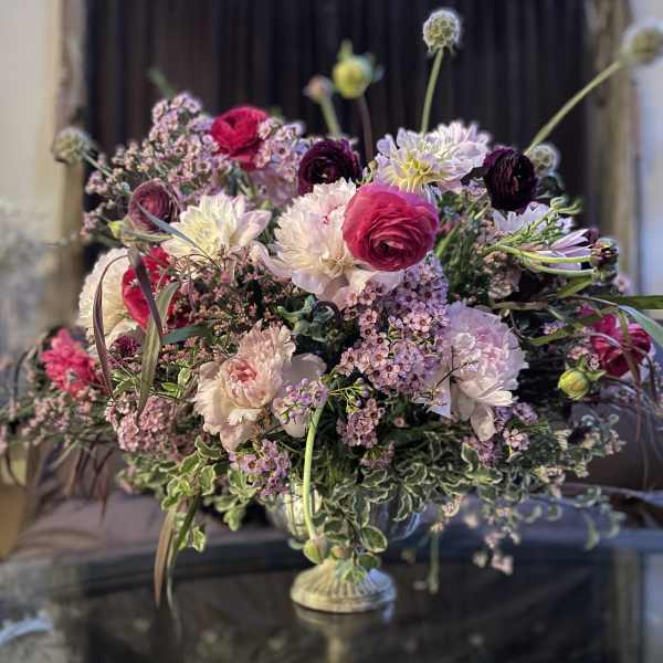 Large mixed floral arrangement in a pedestal vase with pink, white, and purple blooms