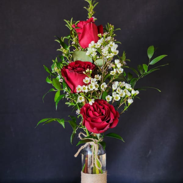 Three red roses in a glass bottle vase with white filler flowers