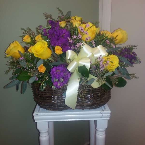 Basket arrangement of yellow roses and purple flowers with a cream ribbon