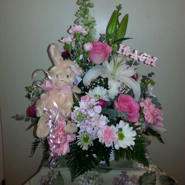Pink and white floral arrangement with a plush bunny and "It's a Girl" sign