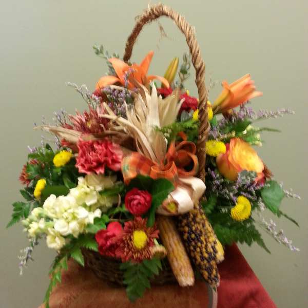 Basket arrangement with mixed flowers, corn, and a rope handle