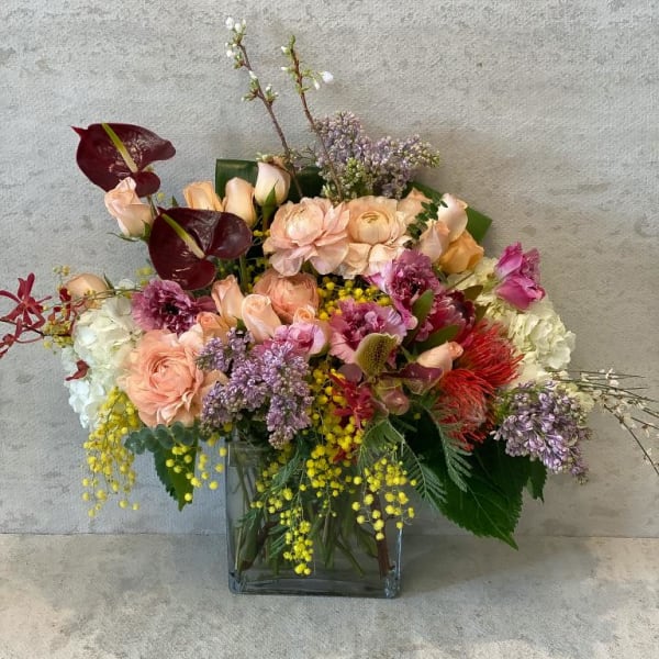 Mixed bouquet in a square glass vase with peach, pink, and purple flowers