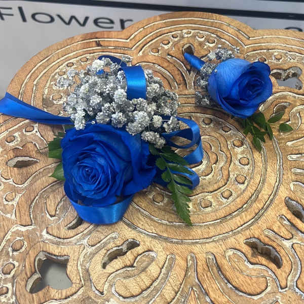 Two blue rose boutonnieres with silver baby's breath and ribbon