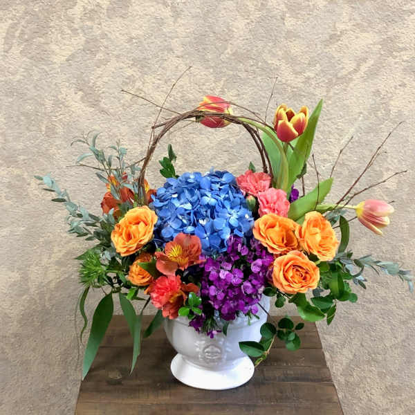 Colorful flower arrangement in a white pedestal vase with a twig handle