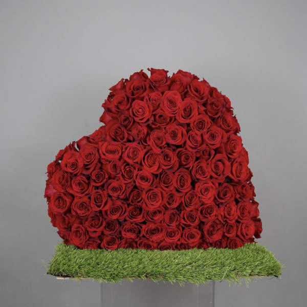 Heart-shaped arrangement of red roses on a grass-covered base