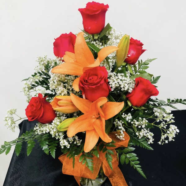 Red roses and orange lilies in a glass vase with an orange ribbon