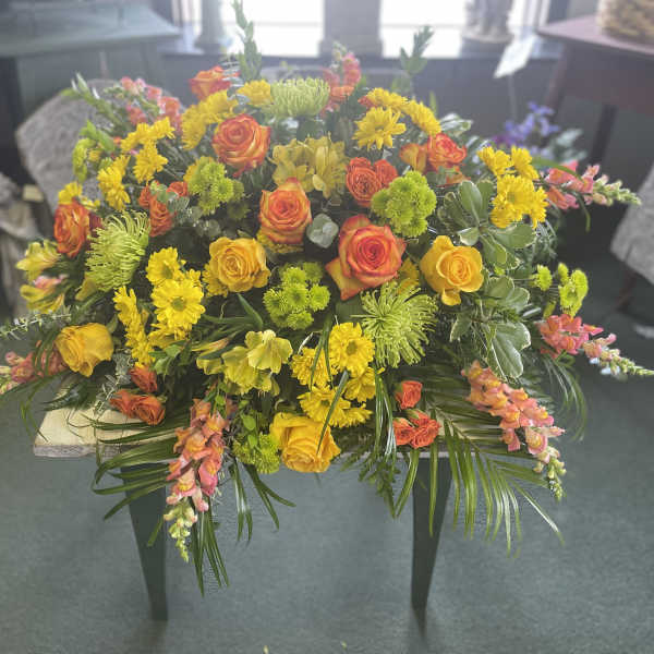 Large bouquet of yellow and orange flowers with greenery on a table