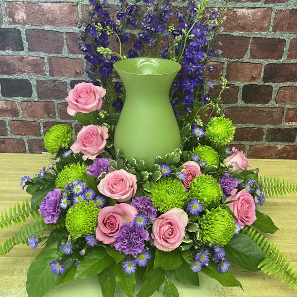 Pink roses and purple flowers arranged around a green vase
