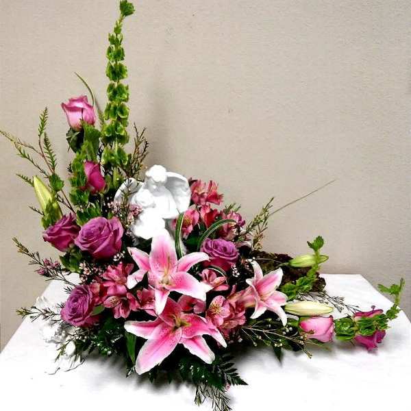 Pink lilies and roses arranged with a white angel figurine