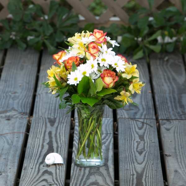 Bouquet of orange roses, white daisies, and yellow flowers in a clear glass vase