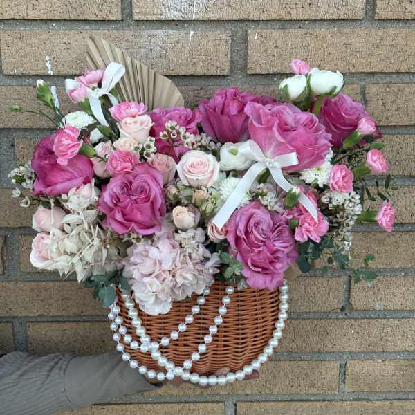 Pink rose bouquet in a wicker basket with white ribbon and pearl strands