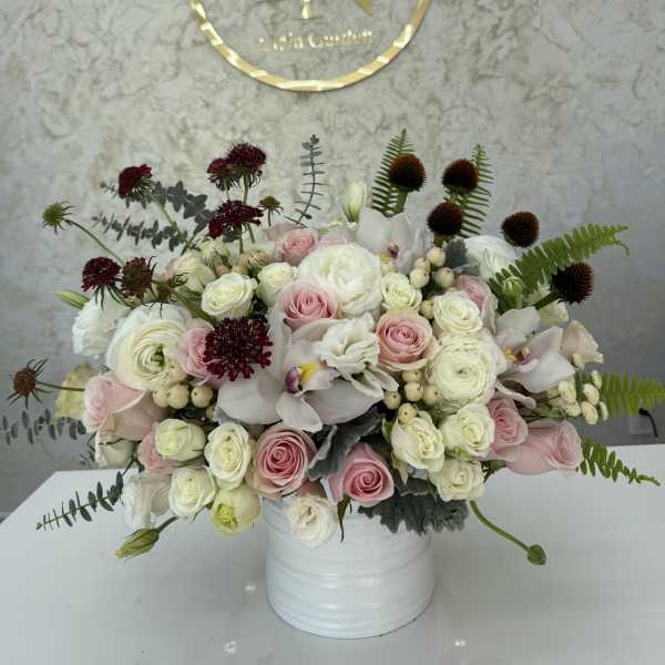 Pink and white rose arrangement in a white vase with dark accent blooms