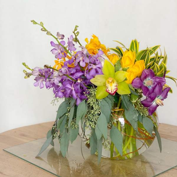 Colorful orchid arrangement in a glass vase with trailing greenery