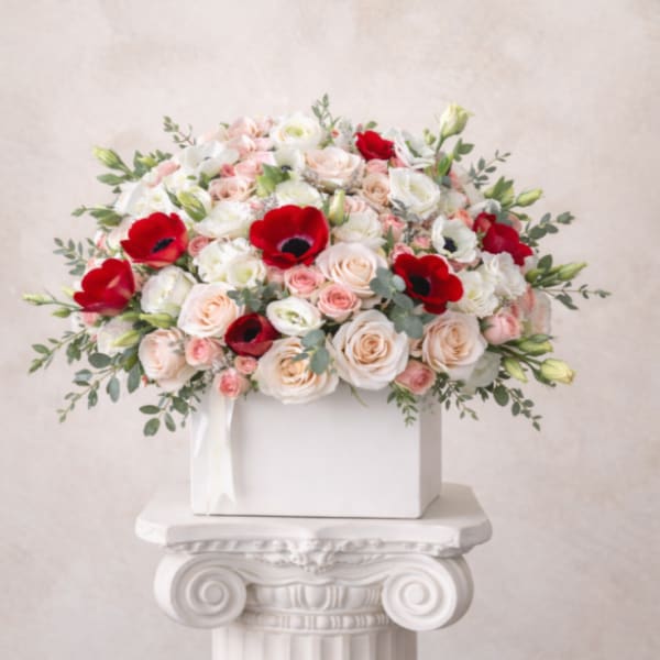 Bouquet of pale roses and red anemones in a white box