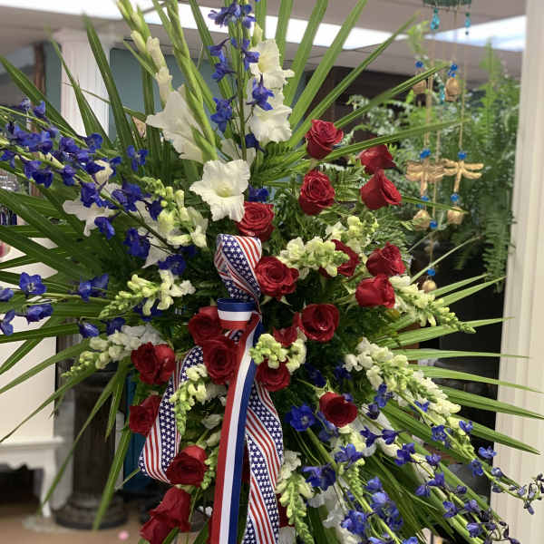 Large standing floral spray with red roses, white flowers, and blue blooms