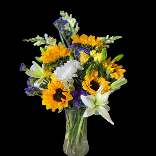 Bouquet of sunflowers, white lilies, and purple filler in a glass vase
