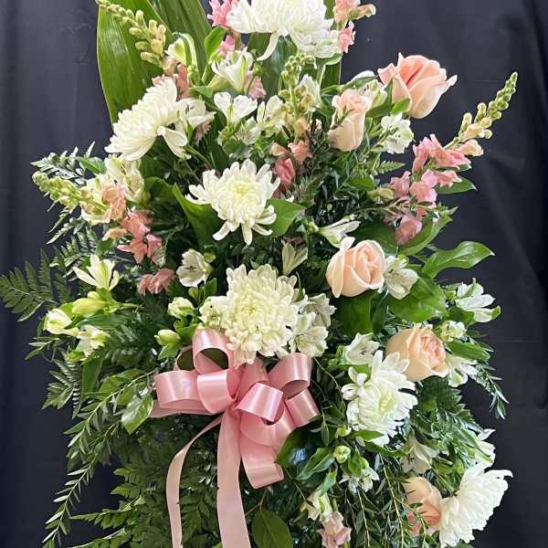 Standing floral spray with white and peach flowers and a pink ribbon