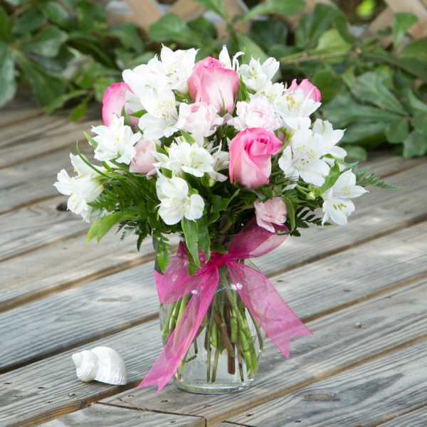 Pink roses and white alstroemeria in a glass vase with a pink ribbon