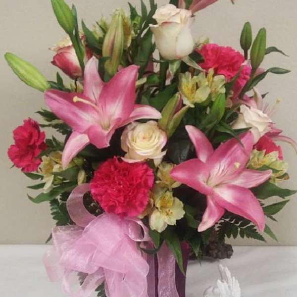 Pink lilies and carnations in a purple vase with a pink ribbon