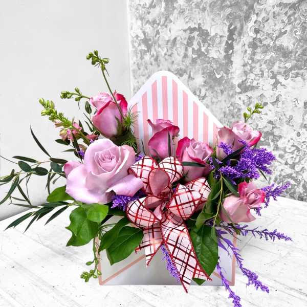 Pink roses in a striped gift box with a red plaid ribbon