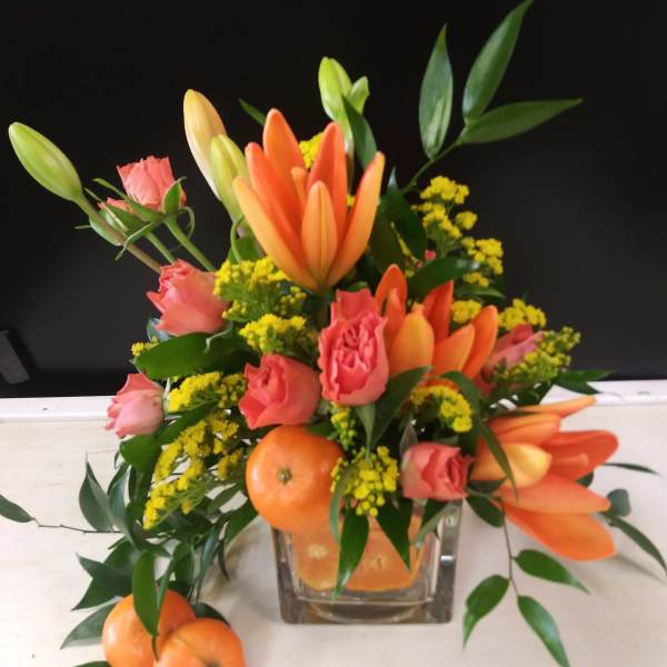 Orange lilies and pink roses in a glass vase with oranges