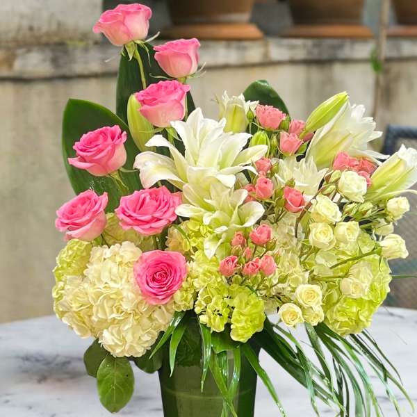 Pink roses and white lilies arranged in a tall green vase