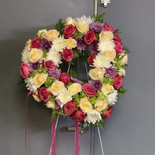 Heart-shaped floral wreath with pink, cream, and purple blooms on a stand