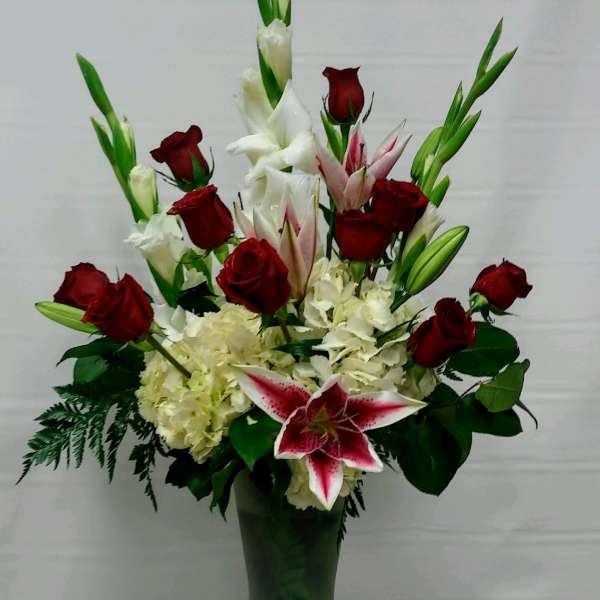 Tall floral arrangement with red roses, white lilies, and pink stargazer lilies in a vase