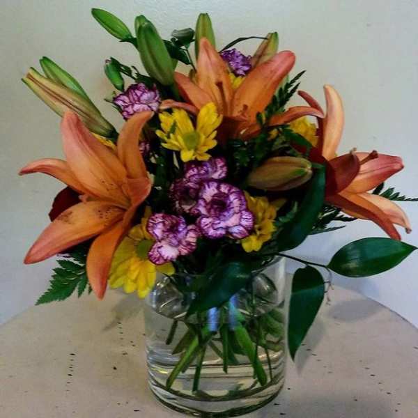 Orange lilies and purple carnations in a clear glass vase