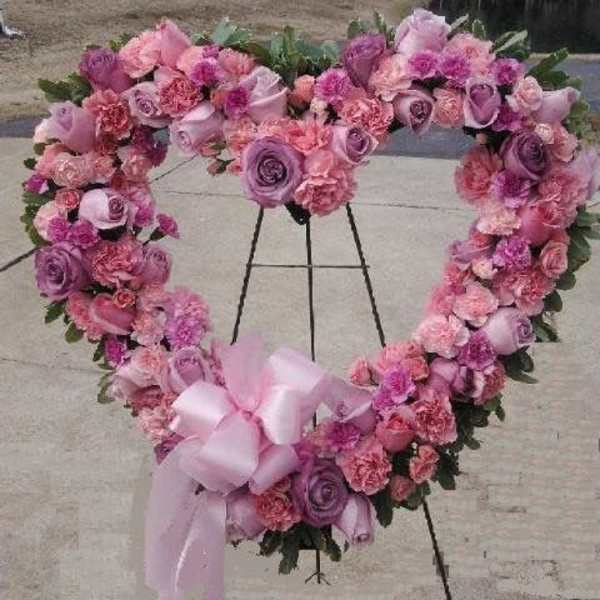 Heart-shaped pink and purple floral wreath on an easel with a ribbon bow