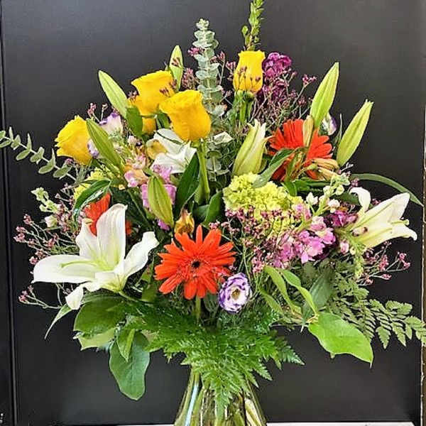 Mixed bouquet of lilies, gerbera daisies, and roses in a glass vase