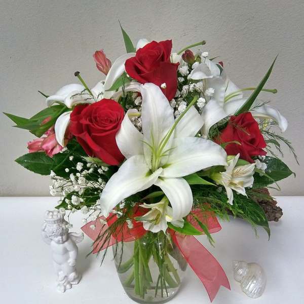 Bouquet of red roses and white lilies in a glass vase with a pink ribbon