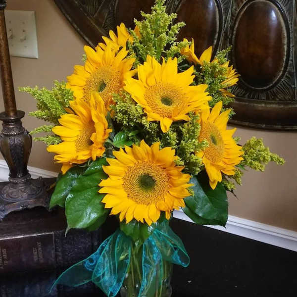 Bouquet of bright yellow sunflowers with a teal ribbon in a glass vase