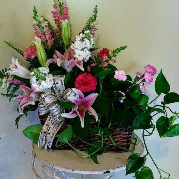 Mixed pink and white floral arrangement in a wicker basket with a ribbon bow