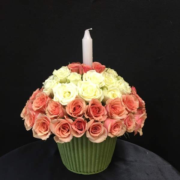 Pink and white rose arrangement in a green vase with a white candle