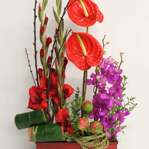 Tall floral arrangement with red anthuriums, gladiolus, and purple orchids in a red container