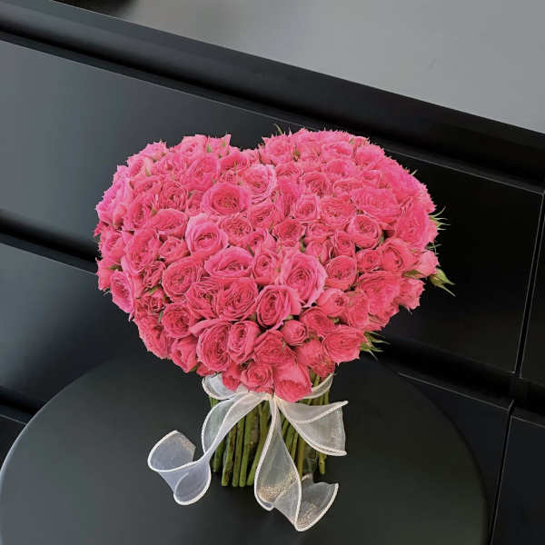 Heart-shaped bouquet of bright pink roses tied with a white ribbon