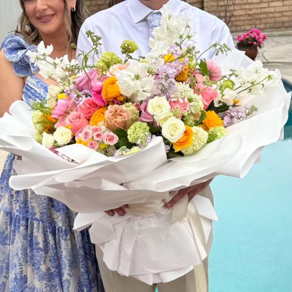 Large bouquet of pink, white, and yellow flowers wrapped in white paper