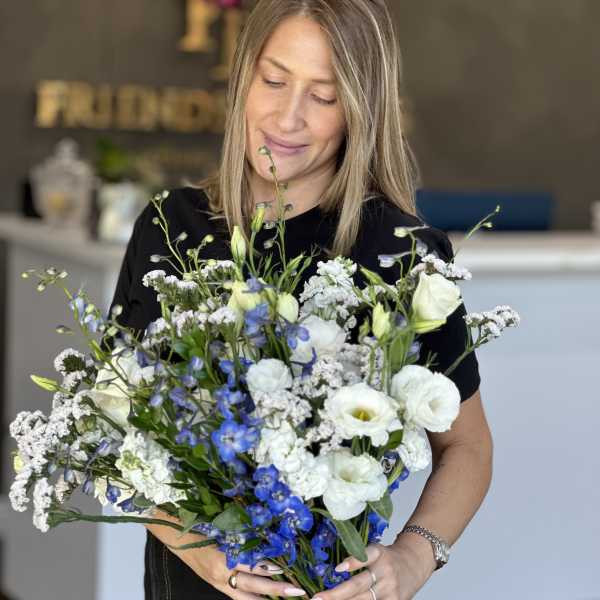 Woman holding a large bouquet of white and blue flowers tied with a satin ribbon.