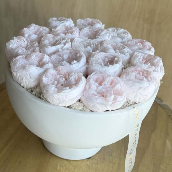 Round box of pale pink peonies with a ribbon tag