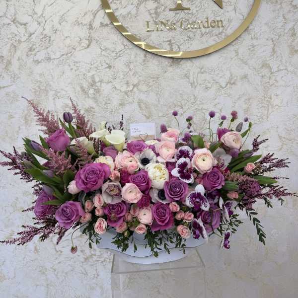 Large bouquet of purple and pink roses with white orchids in a white container