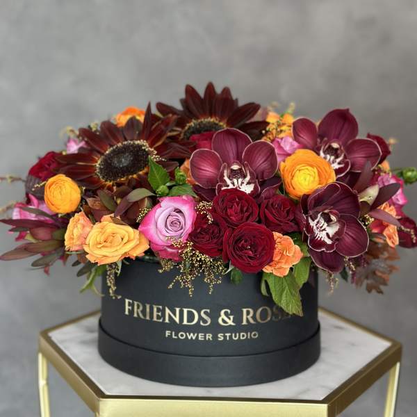 Round box arrangement with burgundy orchids, roses, and sunflowers