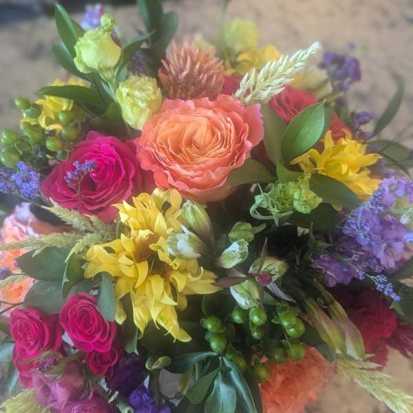 Bright mixed bouquet with peach and hot pink roses, yellow blooms, and purple flowers in a compact arrangement.