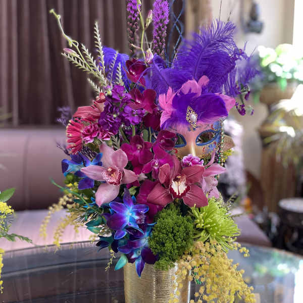 Colorful bouquet with orchids, feathers, and a decorative mask in a gold vase