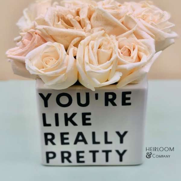 Cream roses in a white square vase with black text