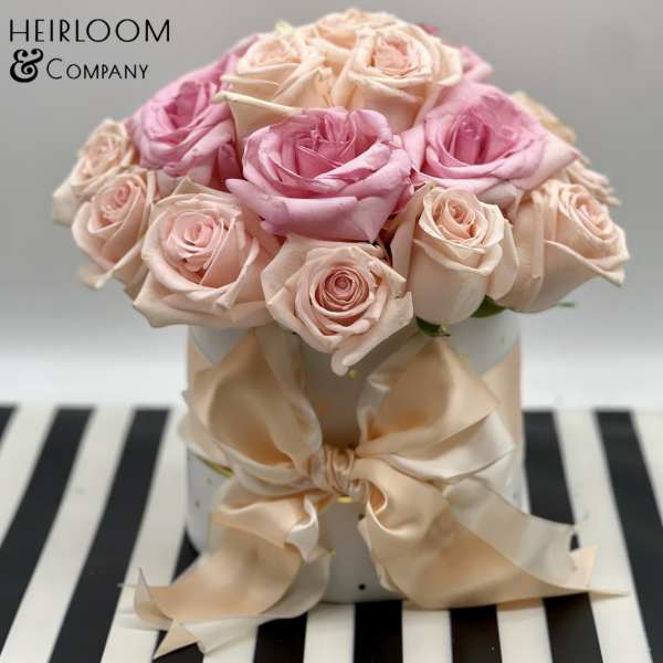 Pink and blush roses arranged in a white hat box with a satin bow