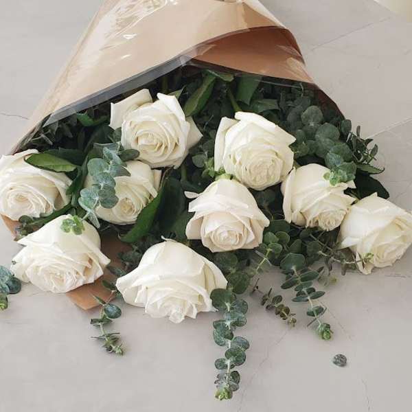 Bouquet of long-stem white roses with eucalyptus wrapped in tan paper and cellophane